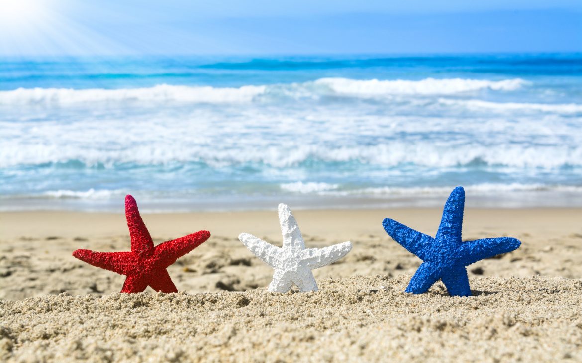 Conceptual summer holiday image of three red, white and blue starfish on the beach overlooking a turquoise ocean while celebrating the July fourth holiday.