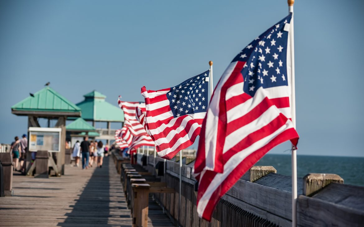Small American flag on a flagpole blowing in the wind at the beach on a pier in Charleston, South Carolina