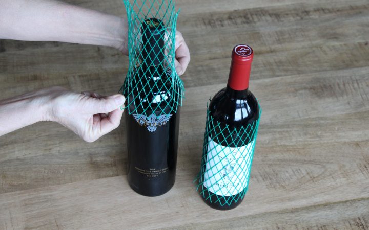 Fastening protective netting over bottles of red wine.