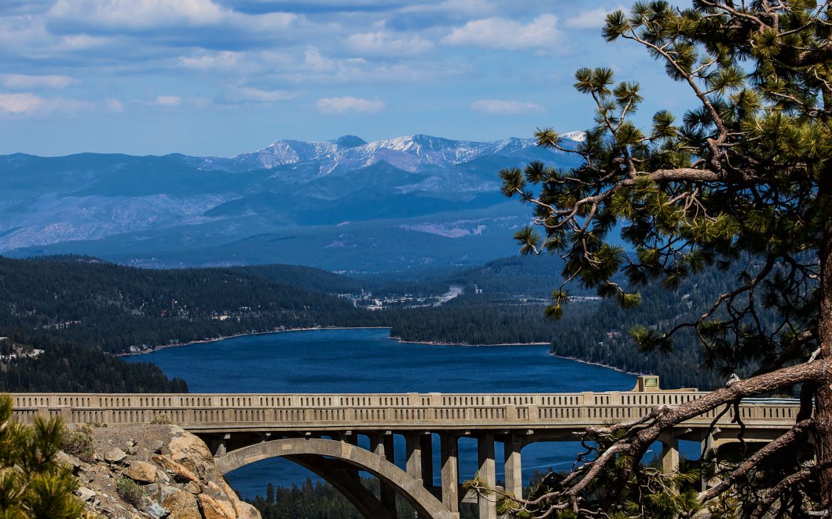 Scenic view of the Donner Memorial Bridge at Donner Pass at the Summit with gorgeous snow capped mountains in the distance and the blue waters of Donner Lake beneath the bridge