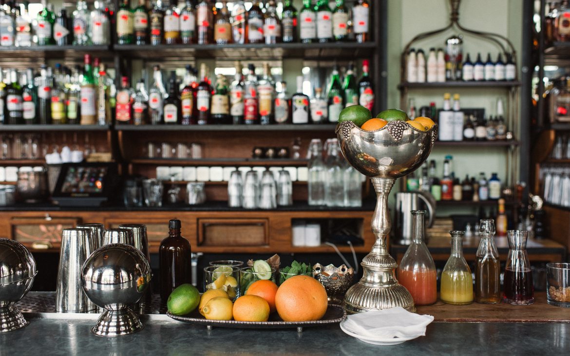 Beautiful bar with silver fixtures and botanical liquors in background and fruit
