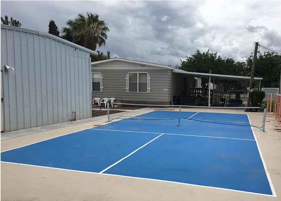 Blue tennis court with gray building in background
