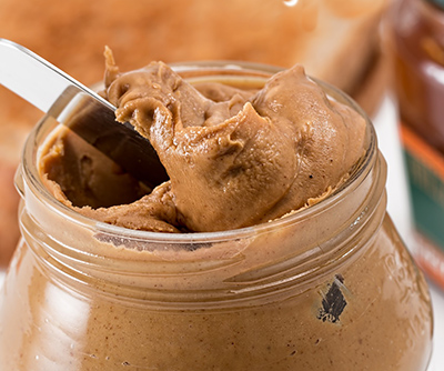 A knife slices into an open jar of peanut butter.