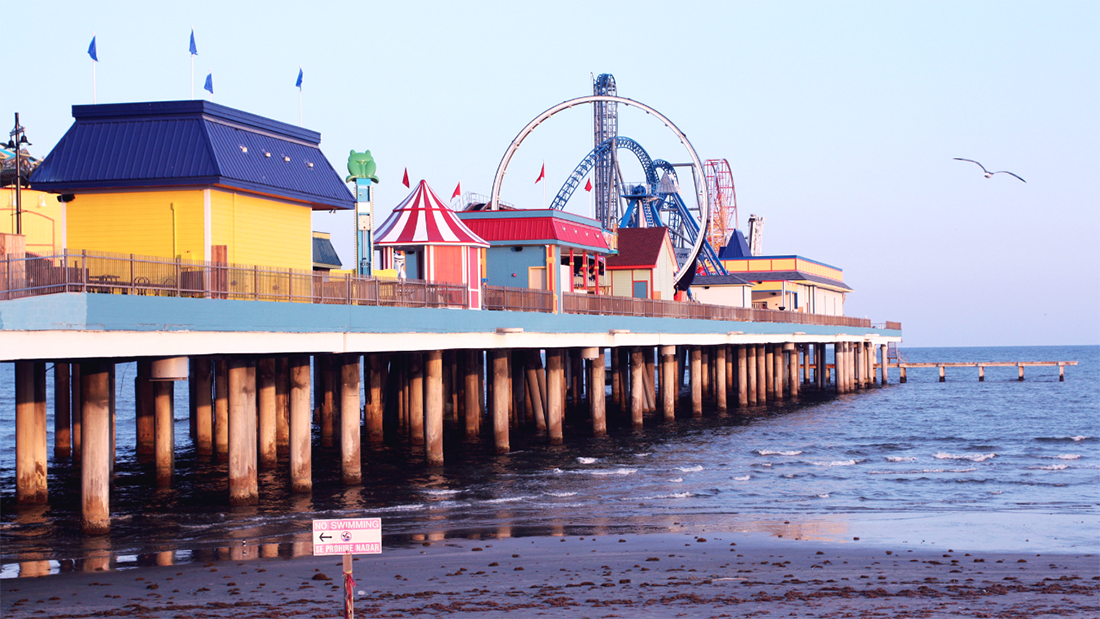 Colorful buildings and amusement park rides sit on an ocean pier in Galveston, Texas.