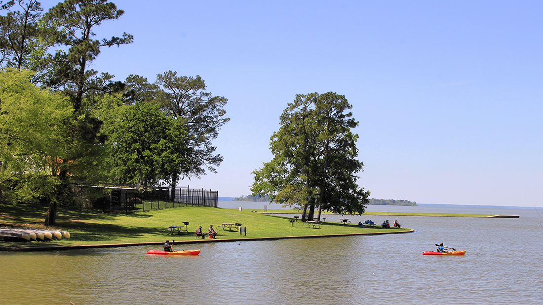 Kayaks launch from a grassy bank on Lake Livingston in Texas.
