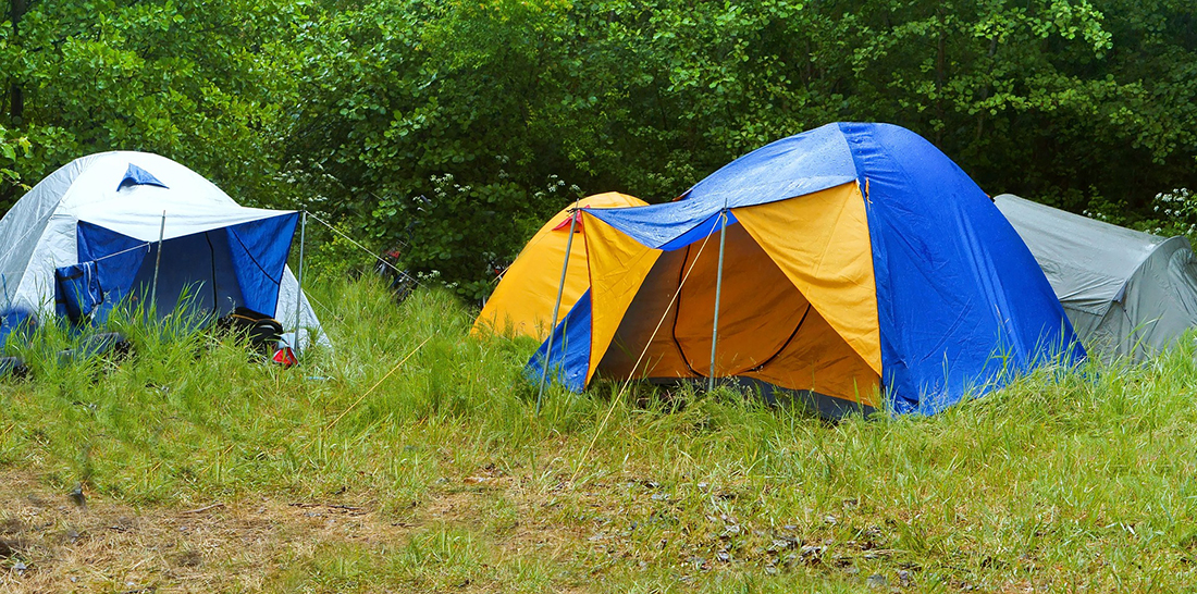Tents camped in a muddy field in the rain.