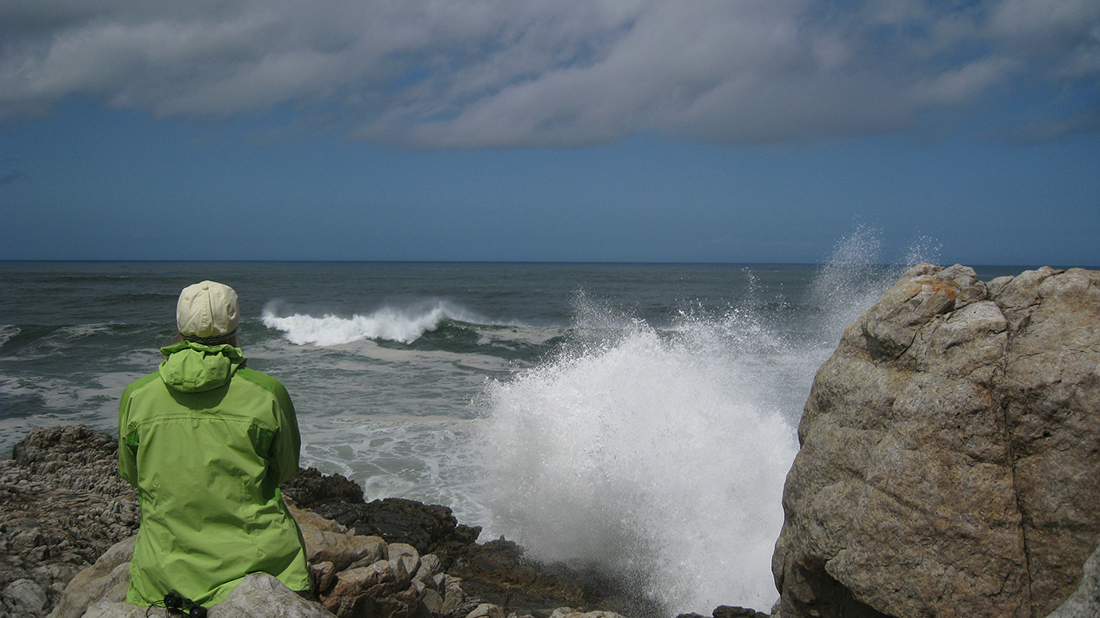 Camper in a green jacket enjoys watching the surf.