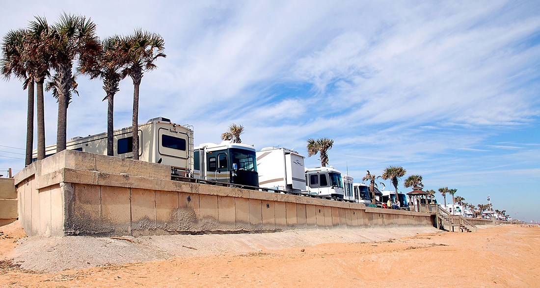 Motorhomes line the beach on a coastal campground.