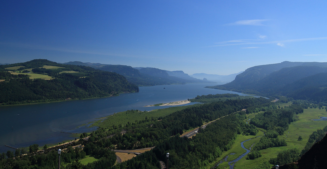 The Columbia River surrounded by bluffs on both side under a blue sky at the Oregon/Washington border.