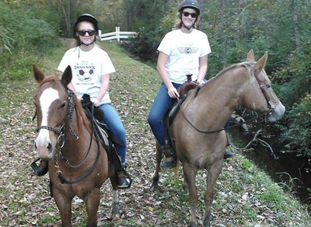 Women on brown horses on dry leave covered trail