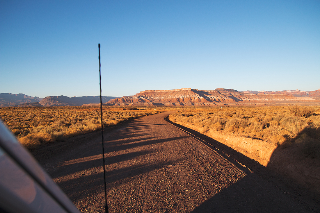 Passenger's view of driving an unpaved road through the desert with bluffs lining the horizon.