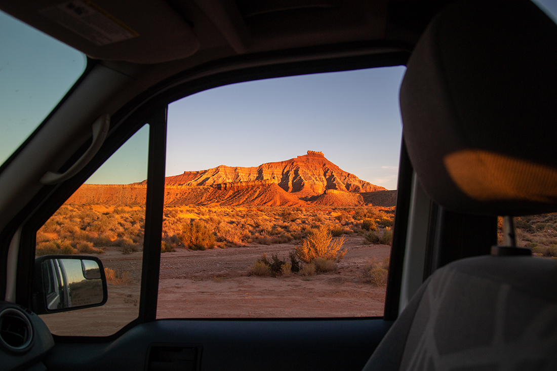 The sunset view of a desert mountain from a vehicle's passenger window.