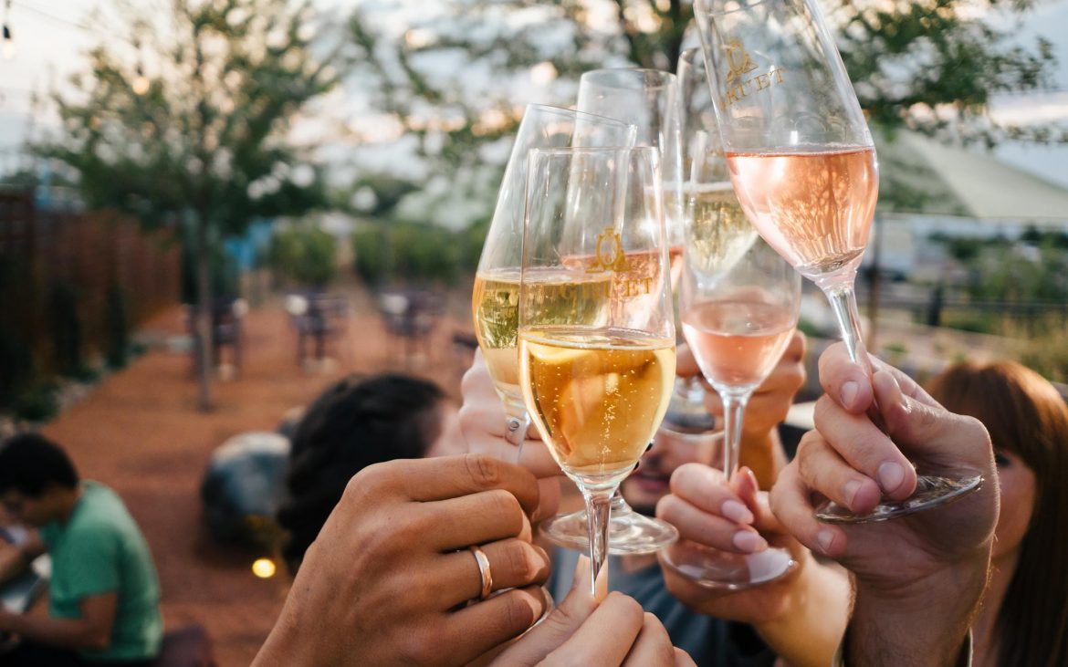 Several hands toasting champagne outside on nice day