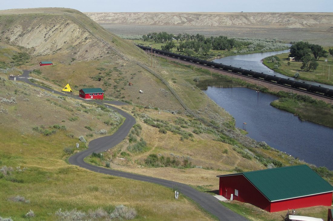 A river winds through a landscape of rolling hills with a red building in the foreground.