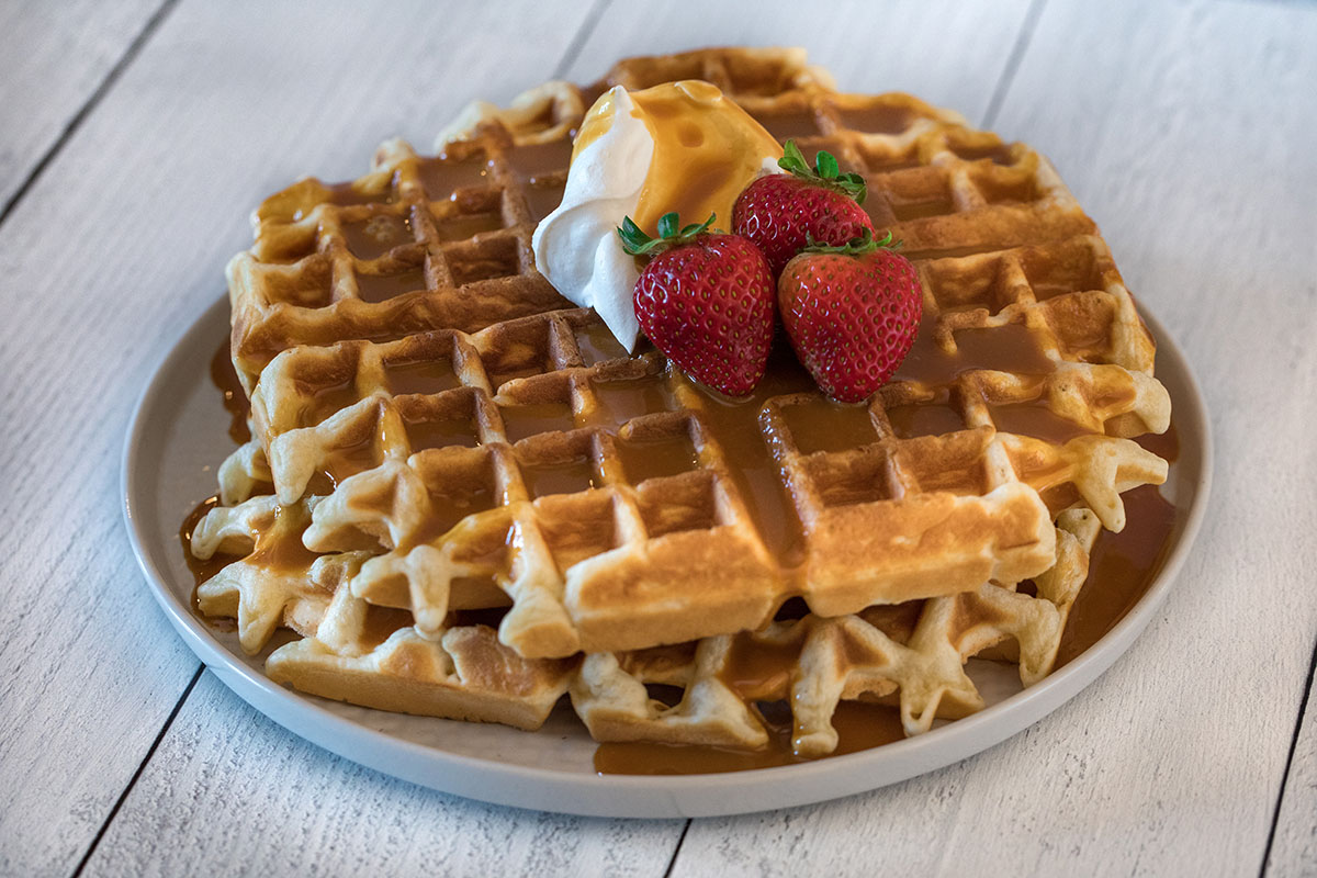 Strawberries, whipped cream and caramel syrup top a stack of waffles.