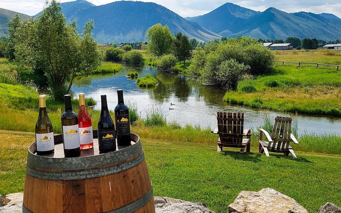 Wine barrel with five bottles outside with stream and mountains in background