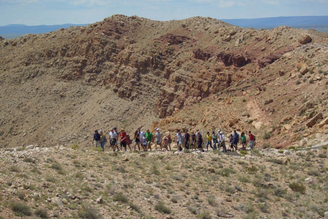 A group of about 20 people hike along the rim of Meteor Crater.