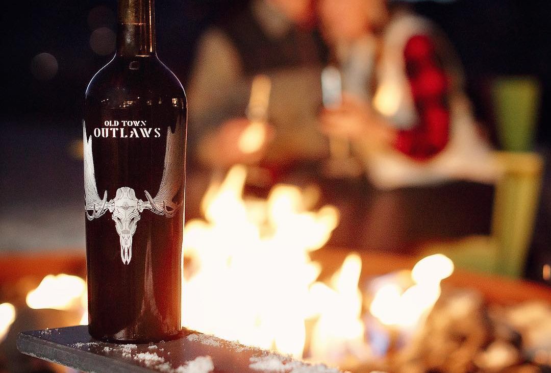Red wine bottle in front of outdoor fire pit and people around it
