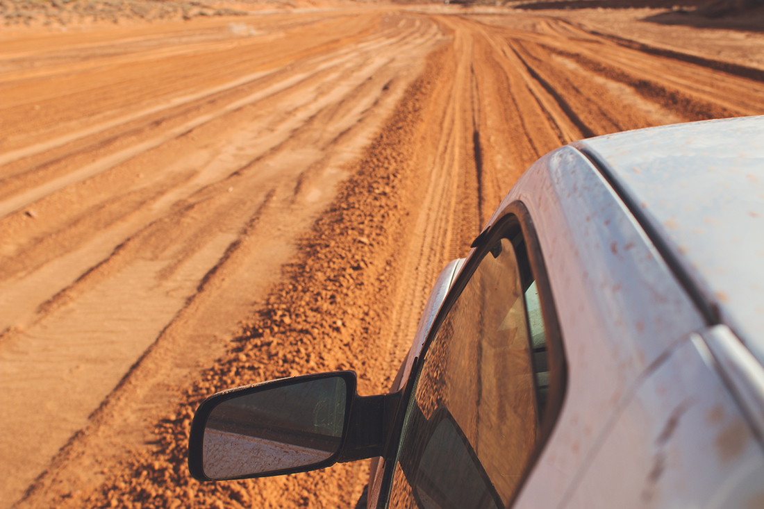 View of driver's side window from above the vehicle with tire track on a dirt road.