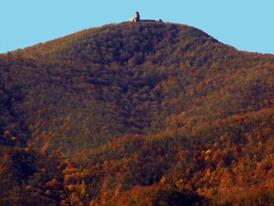 A lone watchtower sits atop a mountain covered in gold and rust foliage.