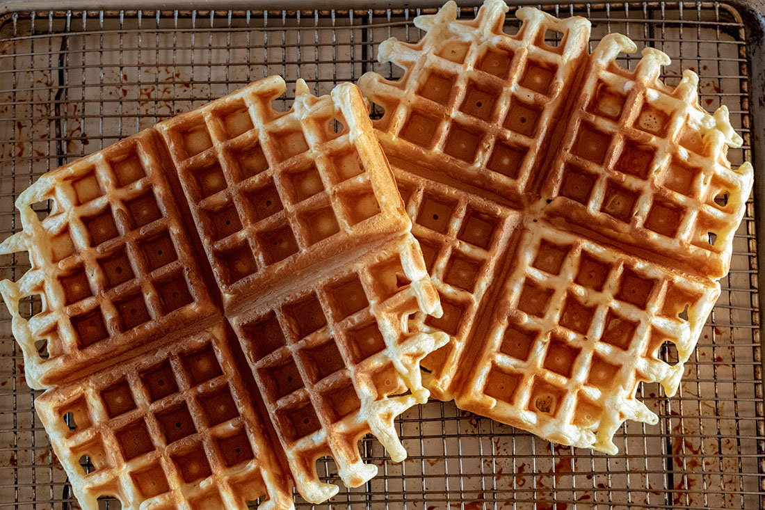 A pair of crispy brown waffles sit atop a wire rack.