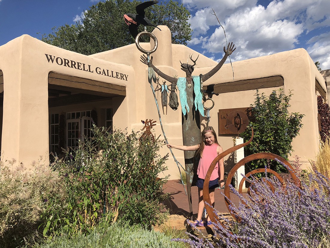 A girl stands in front of a metal sculpture of a Native American spirit at the Worrell Gallery of Santa Fe.