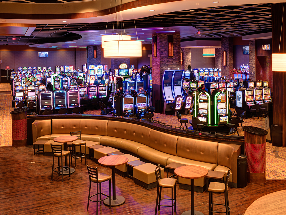 A colorful array of brightly lit slot machines with cocktail tables in the foregroundd.