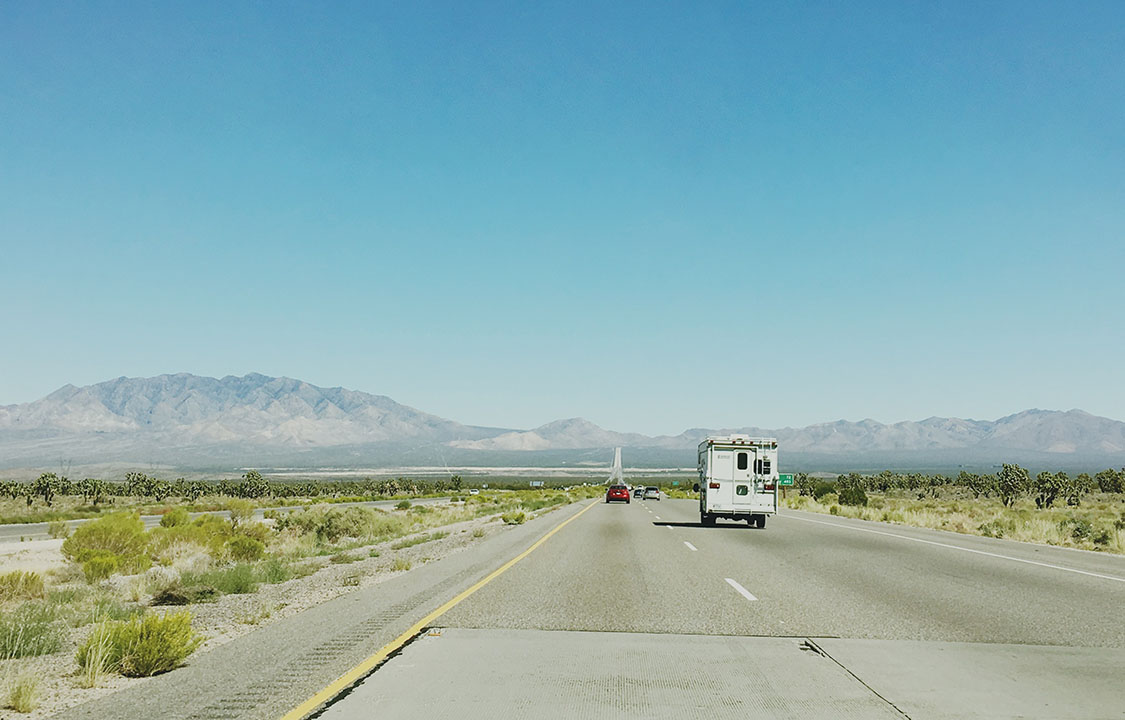 A truck camper rolls down an arid Nevada highway on a clear day.