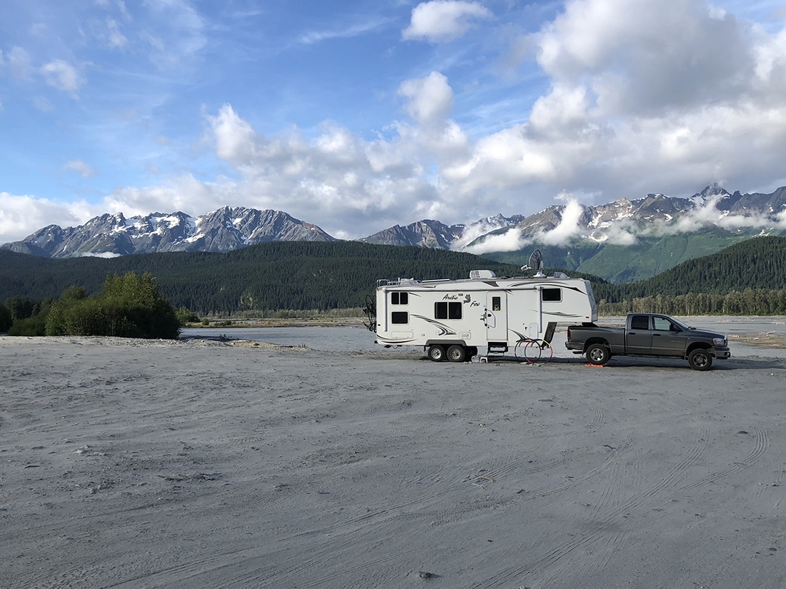 A fifth-wheel trailer parked in the sand with mountains on the horizon.