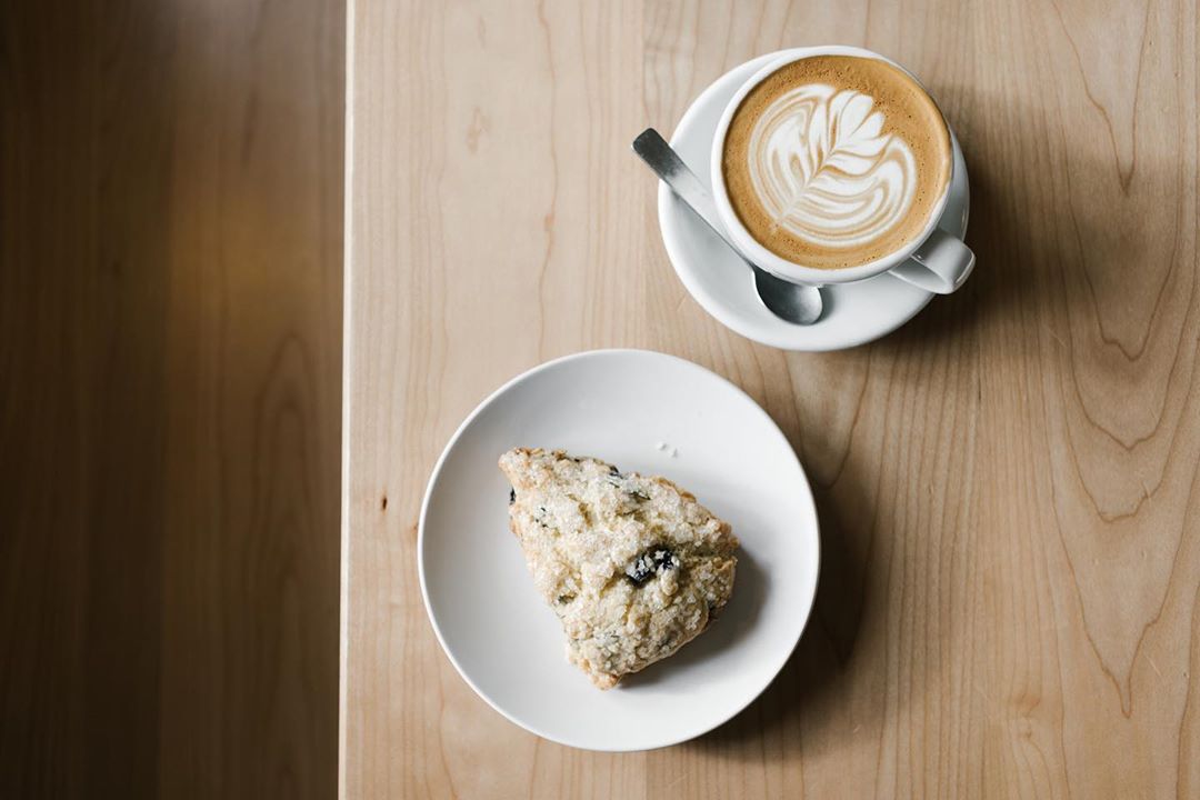 A cup of coffee with a scone on a wooden table.