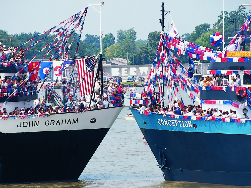 Two ships with patriotic banners and crowds on deck meet bow to bow.