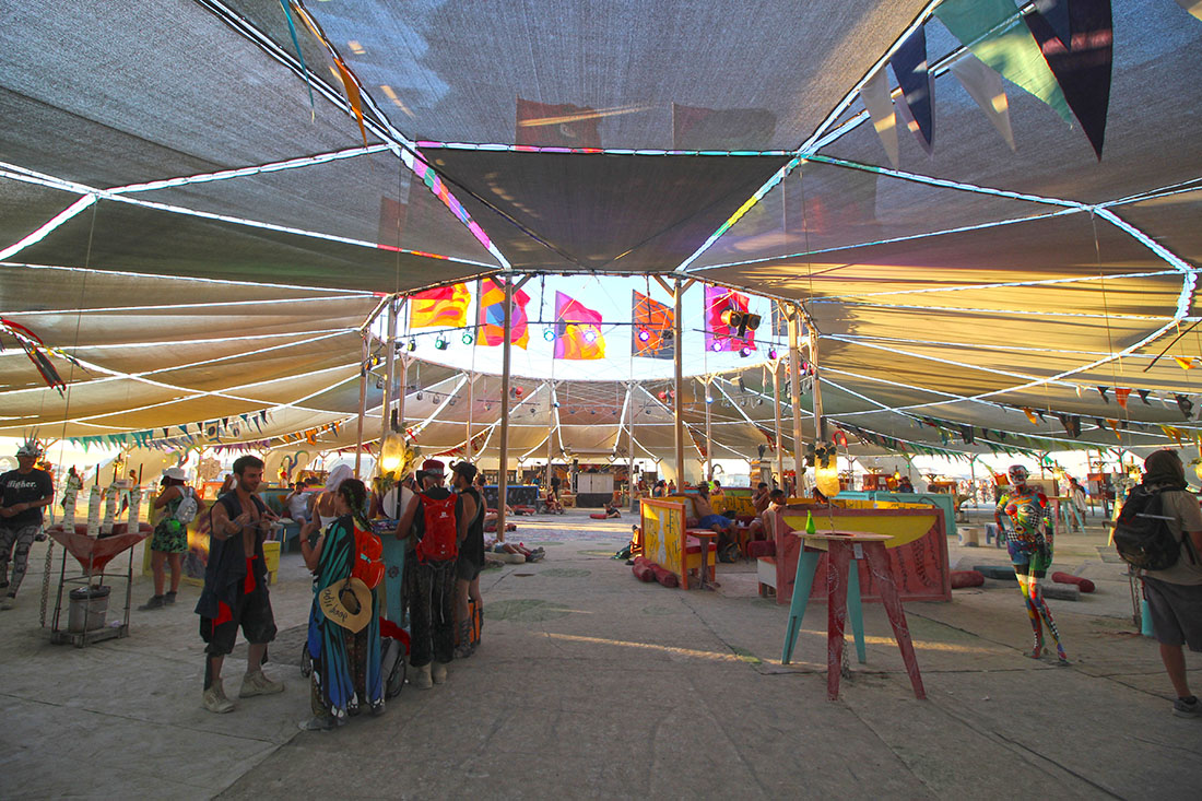 Colorfully dressed event-goers gather under a circular shaped canopy.