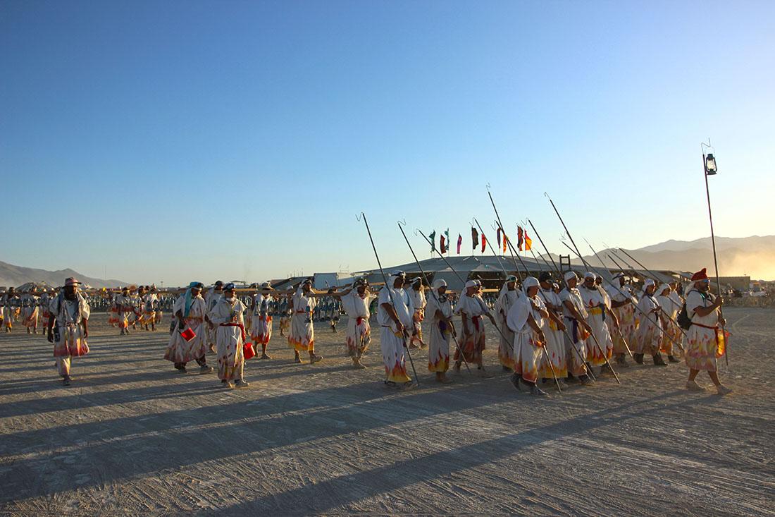 Festival-goers dressed in robed adorned with flame patterns march in formation.