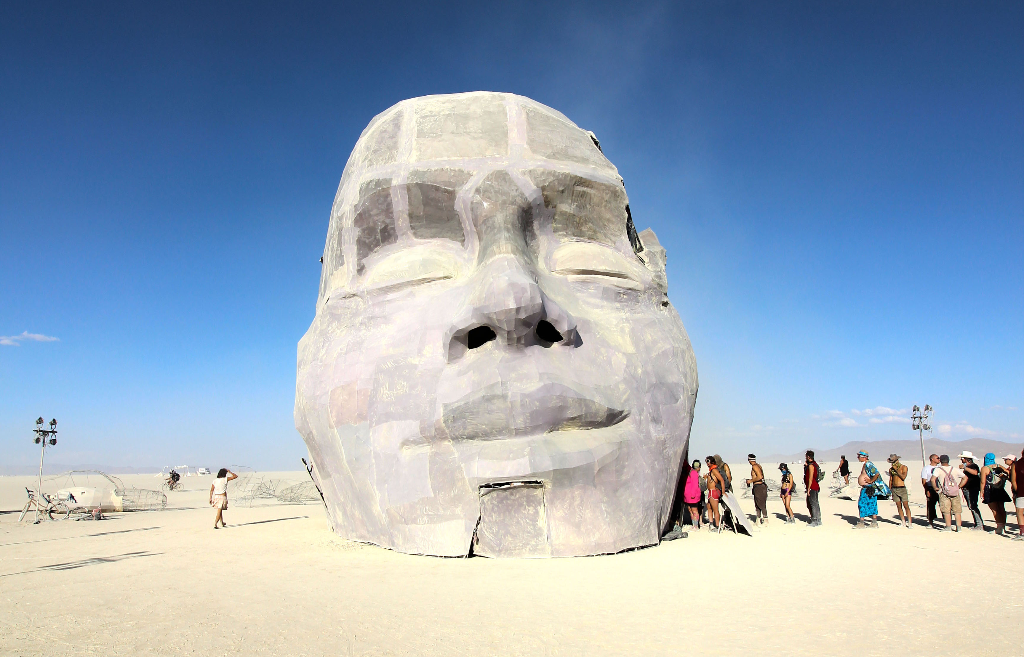 A column of people walk into the sculpture of a 20-foot-tall head that wears a peaceful expression.