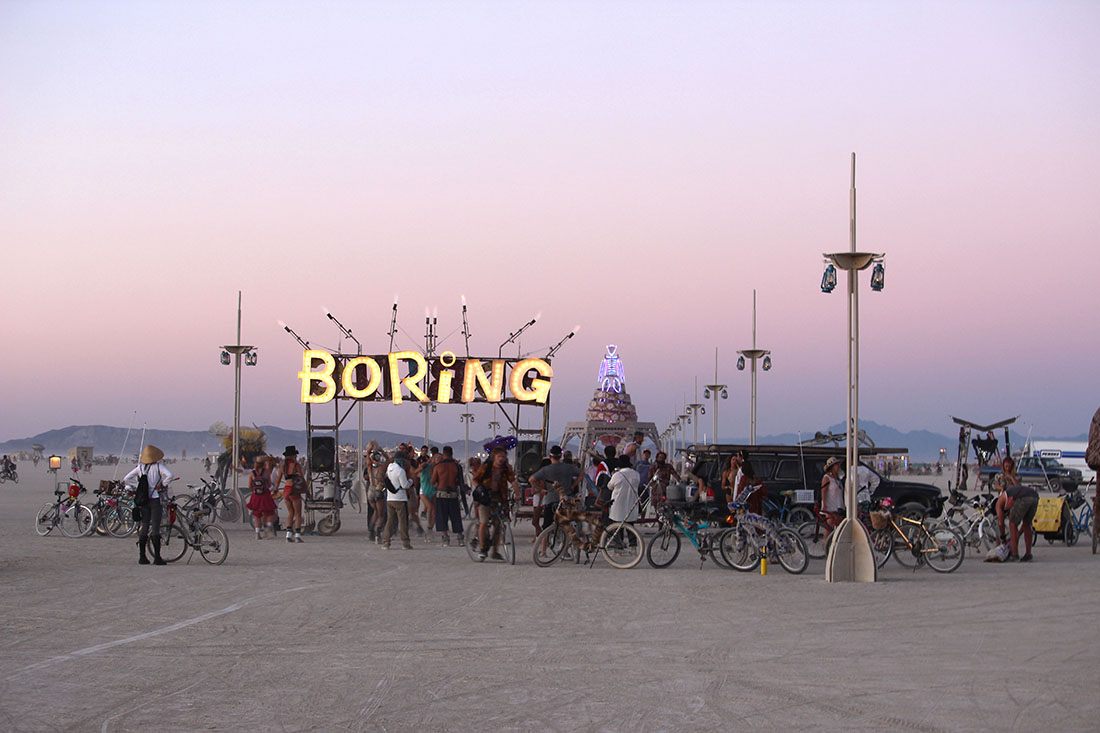 A giant lighted sign hangs over a gathering of bicycle riders and individuals.