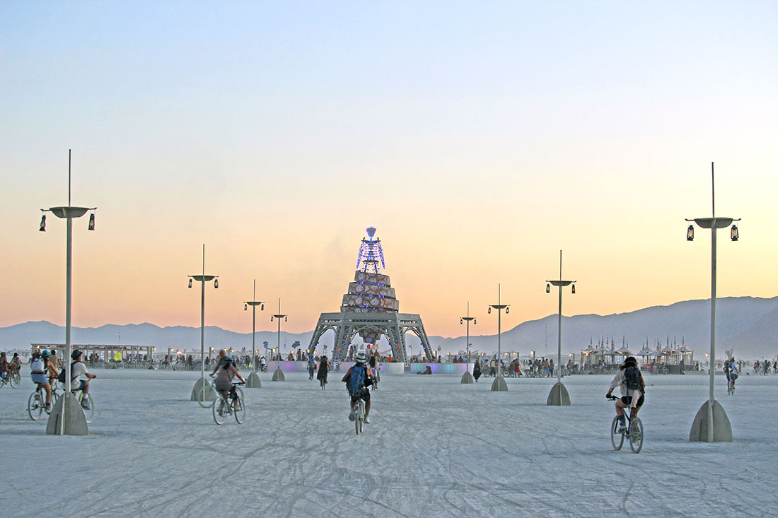 Burning man attendees cycle toward a giant statue of the Burning Man himself.