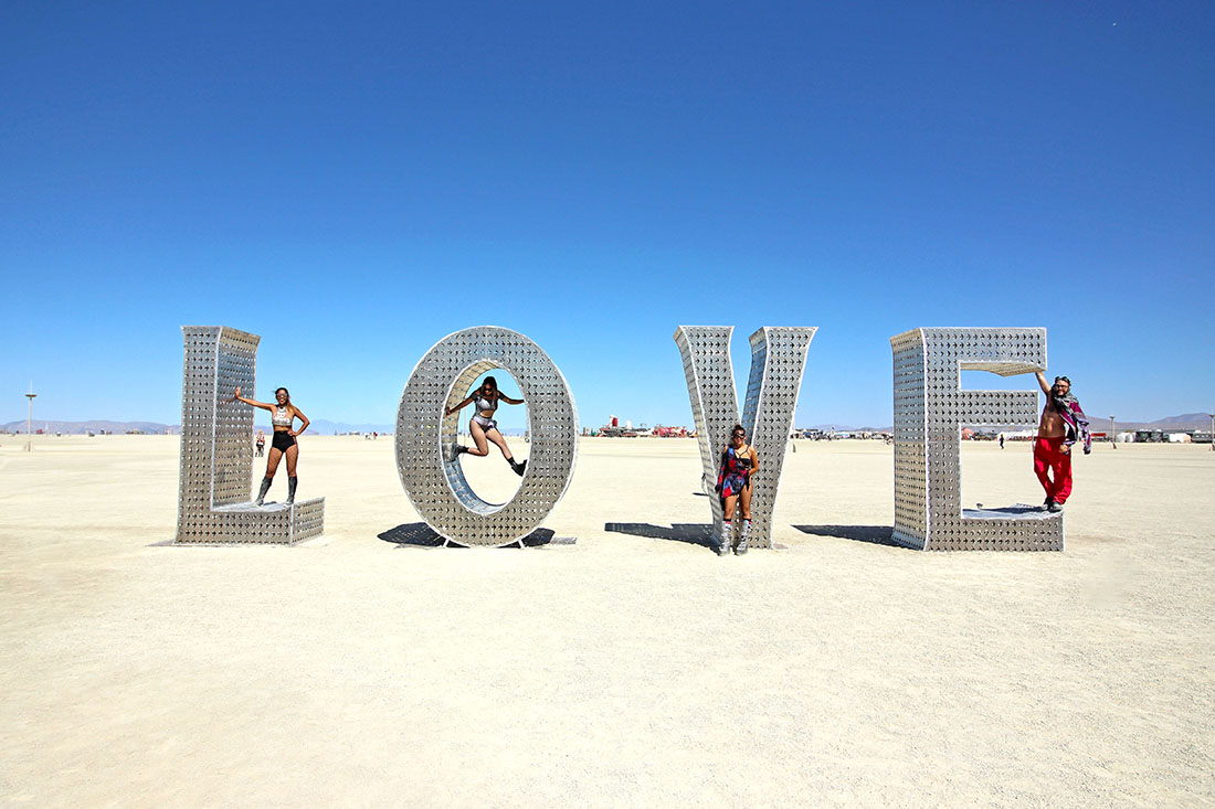 Four colorfully dressed people pose with a giant "love" sculpture.