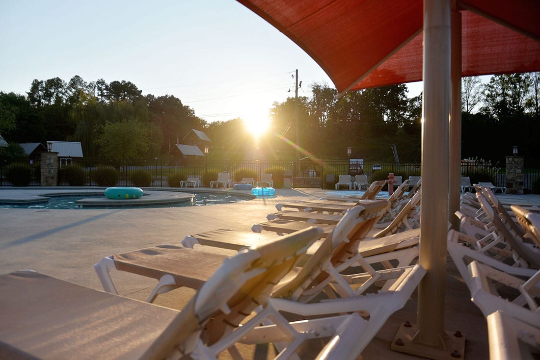 The sunsets over the horizon, shining its last rays on a row of chaise lounges sitting poolside.