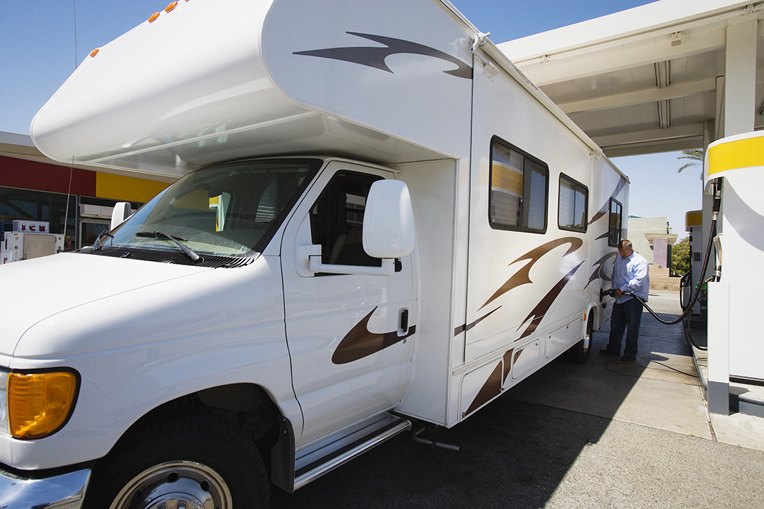 A man refuels a white minimotorhome adorned with teal and brown graphics.