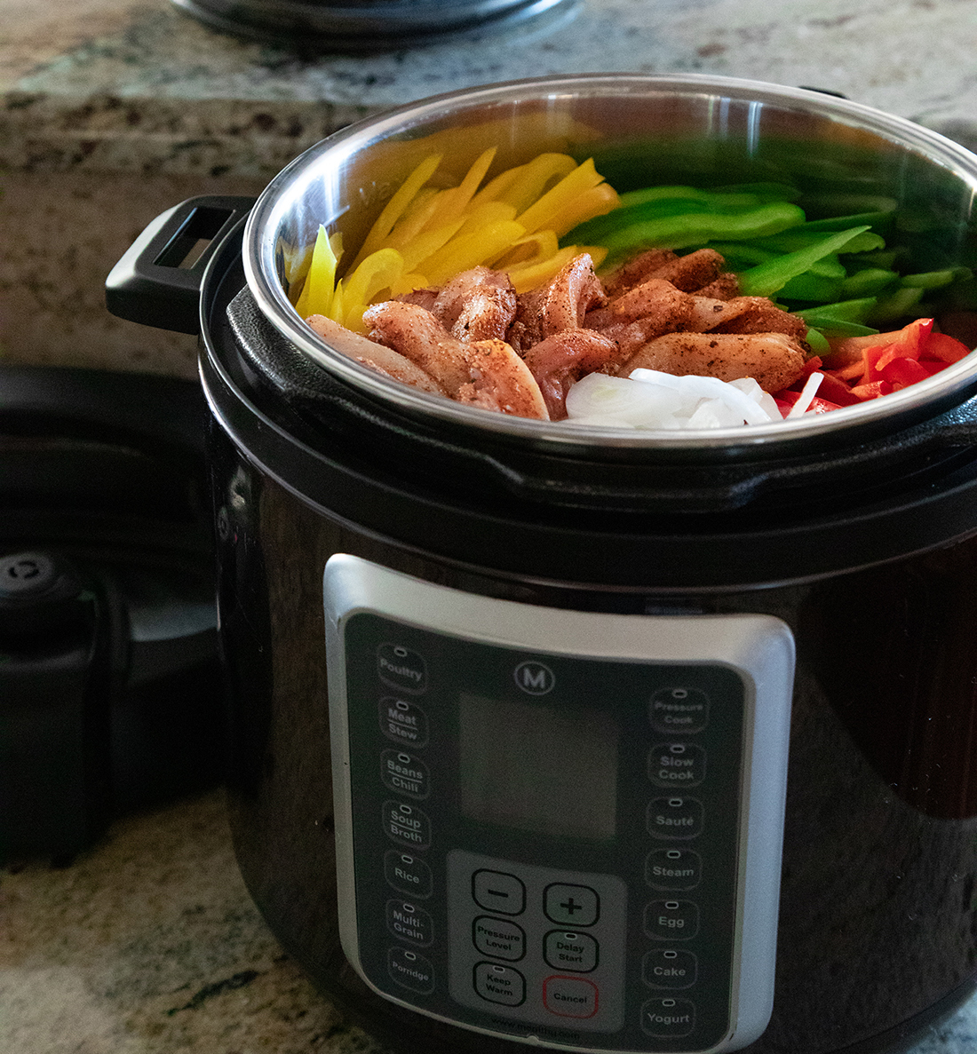 A pressure cooker filled with onions, chicken and red, green and yellow peppers.