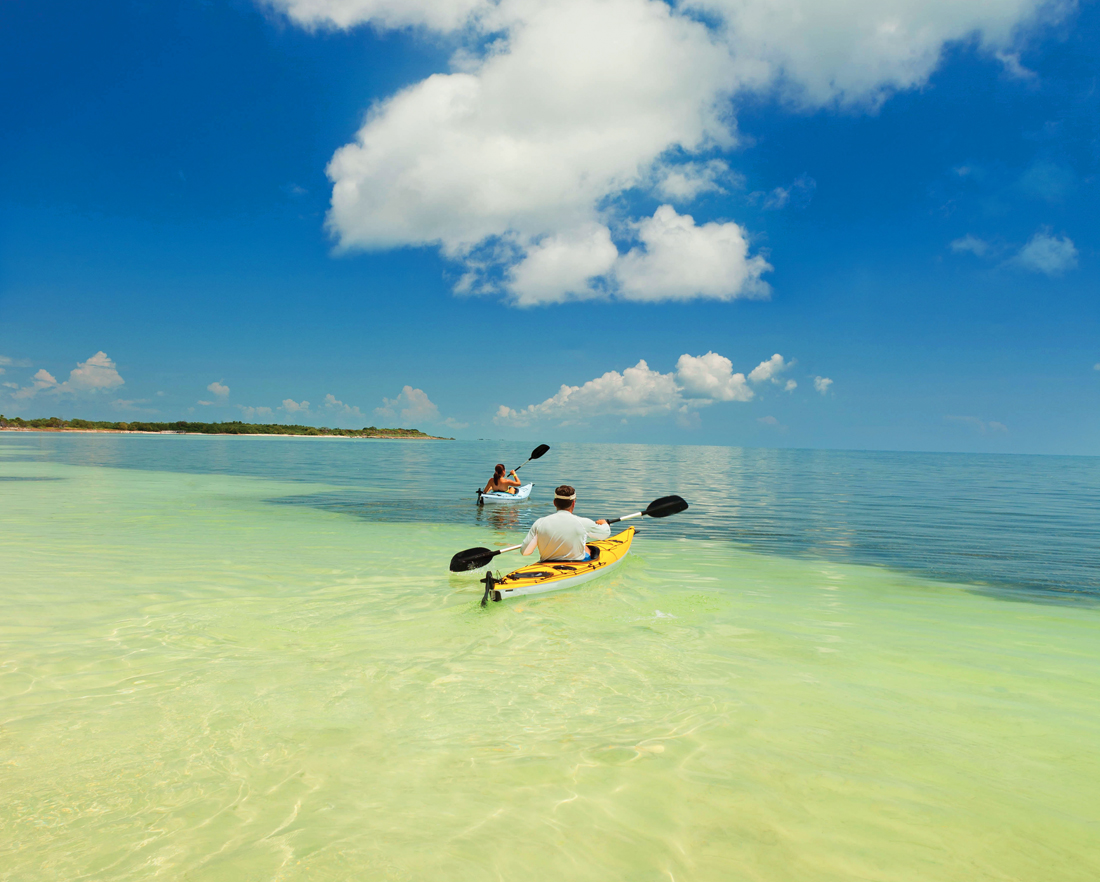 kayaking florida's lower keys A couple paddle in individual kayaks across clear shallow ocean water.