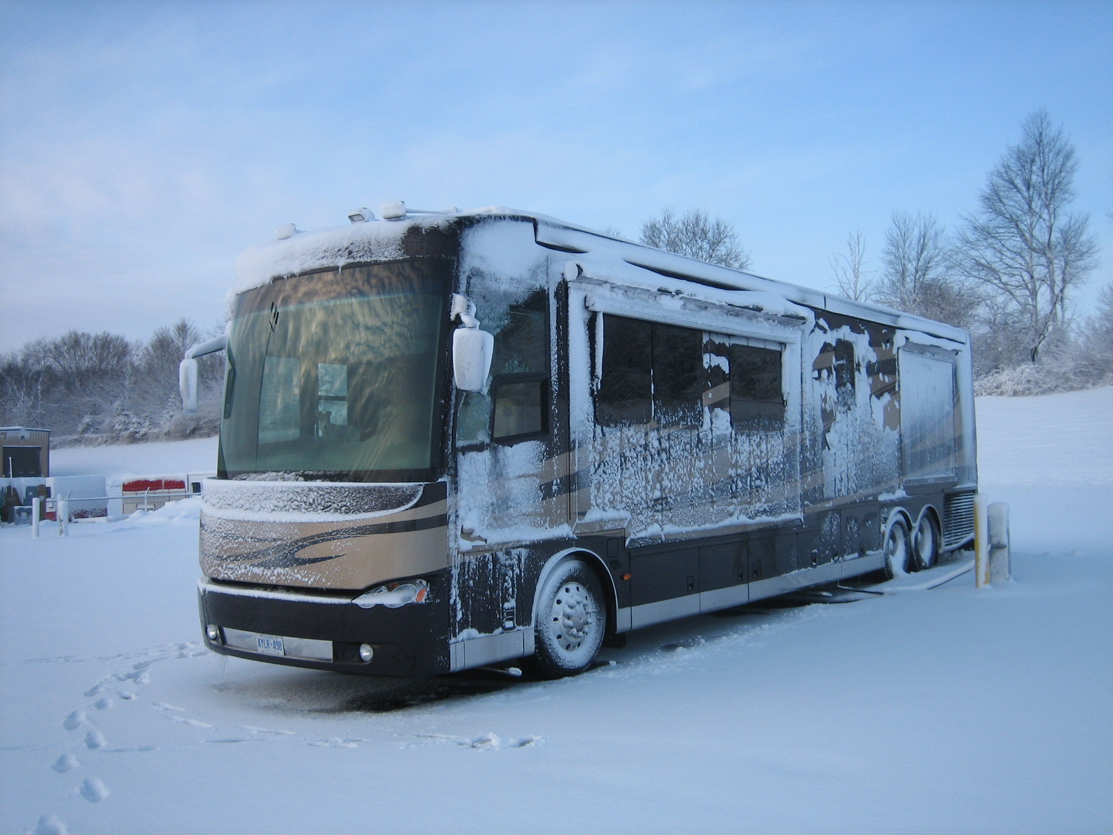 A motorhome sits on a snowby lot encrusted with snow and icicles.