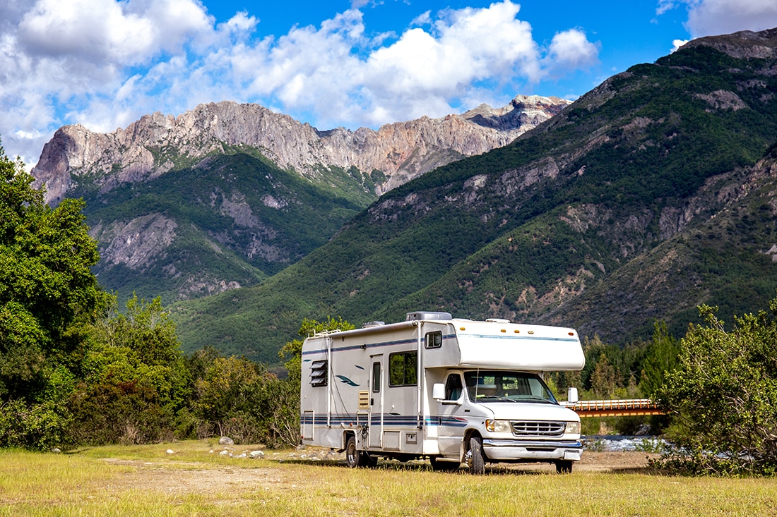 A Class C motorhome parked in an empty field with mountains rising sharply in the background.