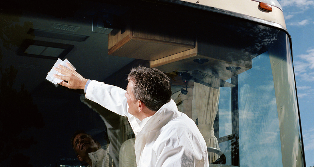 winter rv storage steps — Man cleaning coach bus windshield, side view, under blue sky