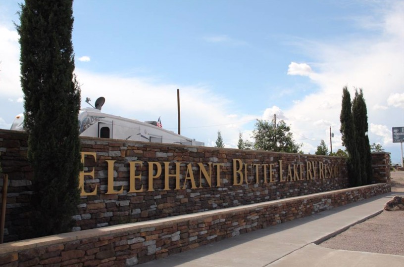 Elephant Butte sign made of metal letters on brick with Italian cypress rising on each side.