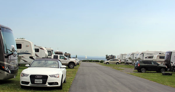 Road inbetween RVs and white Audi parked with water in background