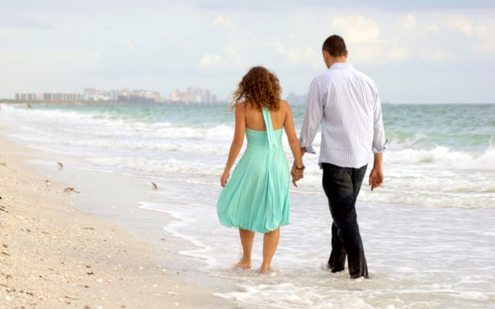 young couple walking hand in hand on the beach thier feet in the