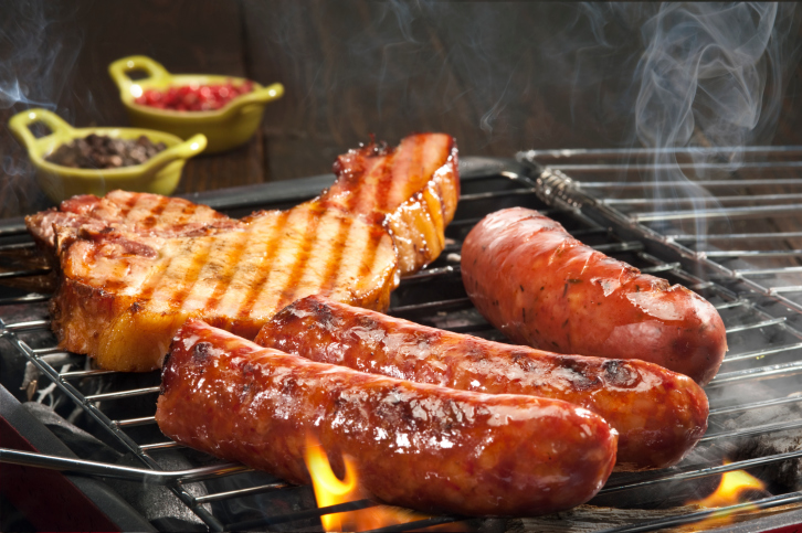 Pork and sausage sizzling on a barbecue grill.
