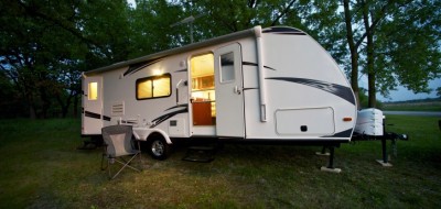 White travel trailer with door open parked on grass and dirt at dusk