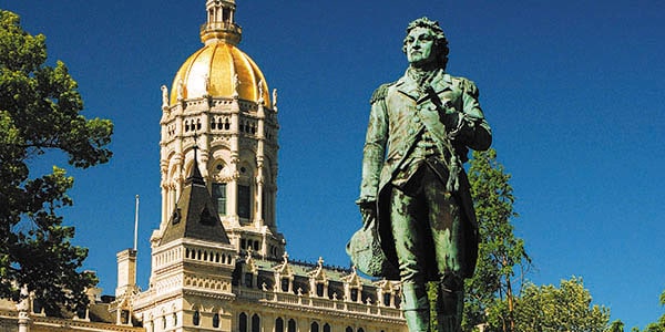 A statue of a man striding purposefully with a golden-domed spire in the background.